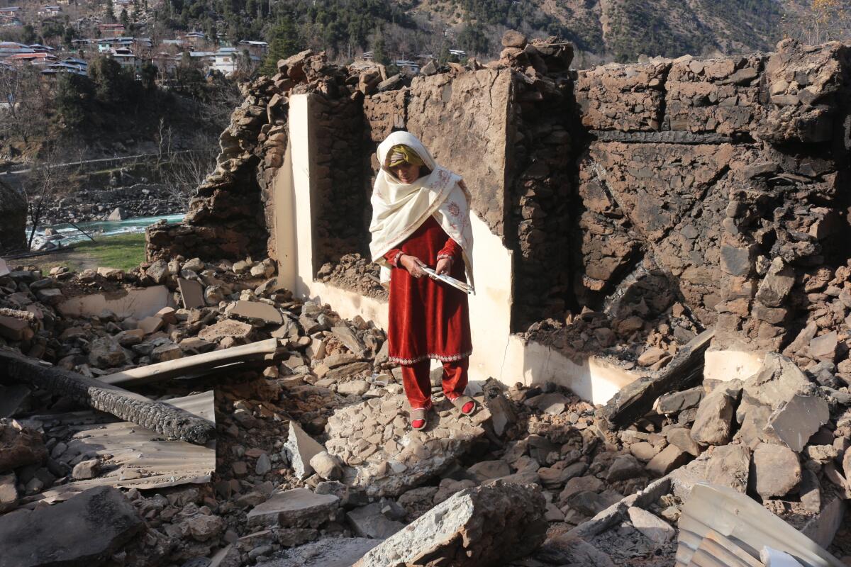 A Pakistani Kashmiri woman stands amid debris of her home that reportedly was destroyed by cross border shelling from Indian troops, in Neelum Valley, situated at the Line of Control in Pakistani Kashmir.