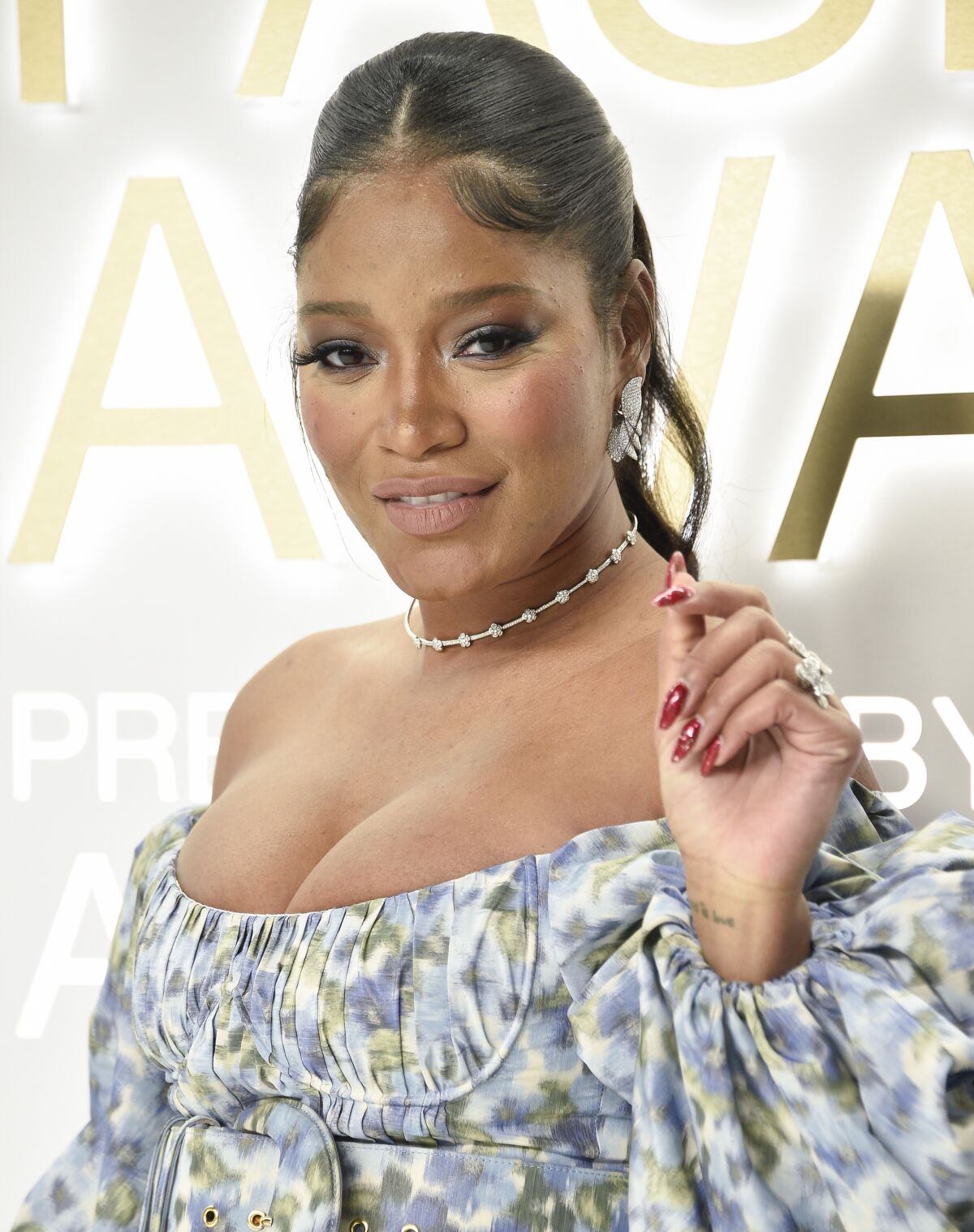 A woman in a blue patterned dress holds up her left hand.