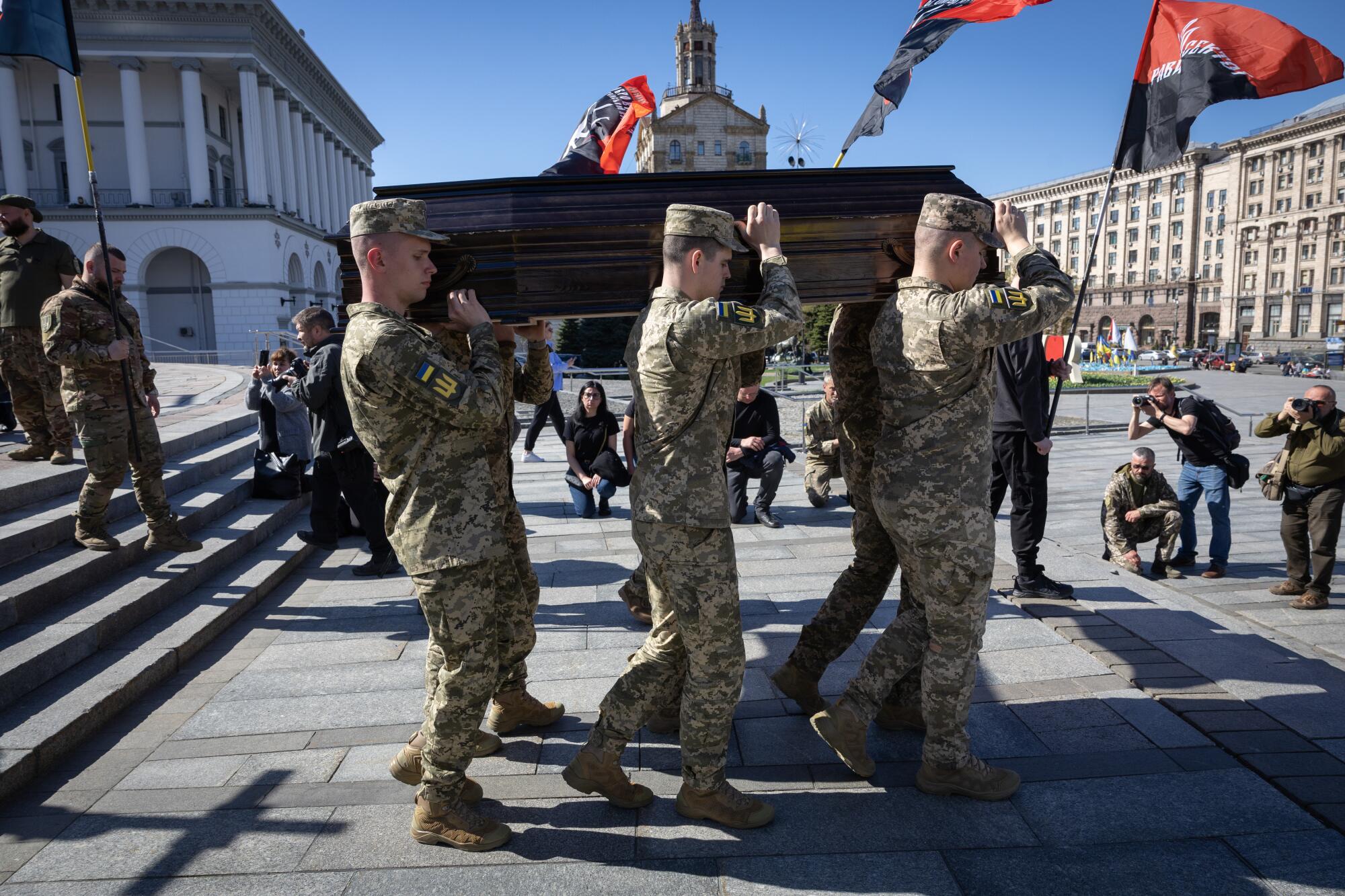 Men in camouflage carry two wooden coffins in a square near people holding red-and-black flags