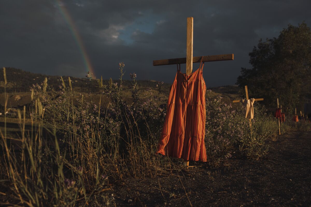 This image provided by World Press Photo which won the World Press Photo Of The Year award by Amber Bracken for The New York Times, titled Kamloops Residential School, shows Red dresses hung on crosses along a roadside commemorate children who died at the Kamloops Indian Residential School, an institution created to assimilate Indigenous children, following the detection of as many as 215 unmarked graves, Kamloops, British Columbia, 19 June 2021. (Amber Bracken for The New York Times/World Press Photo via AP)