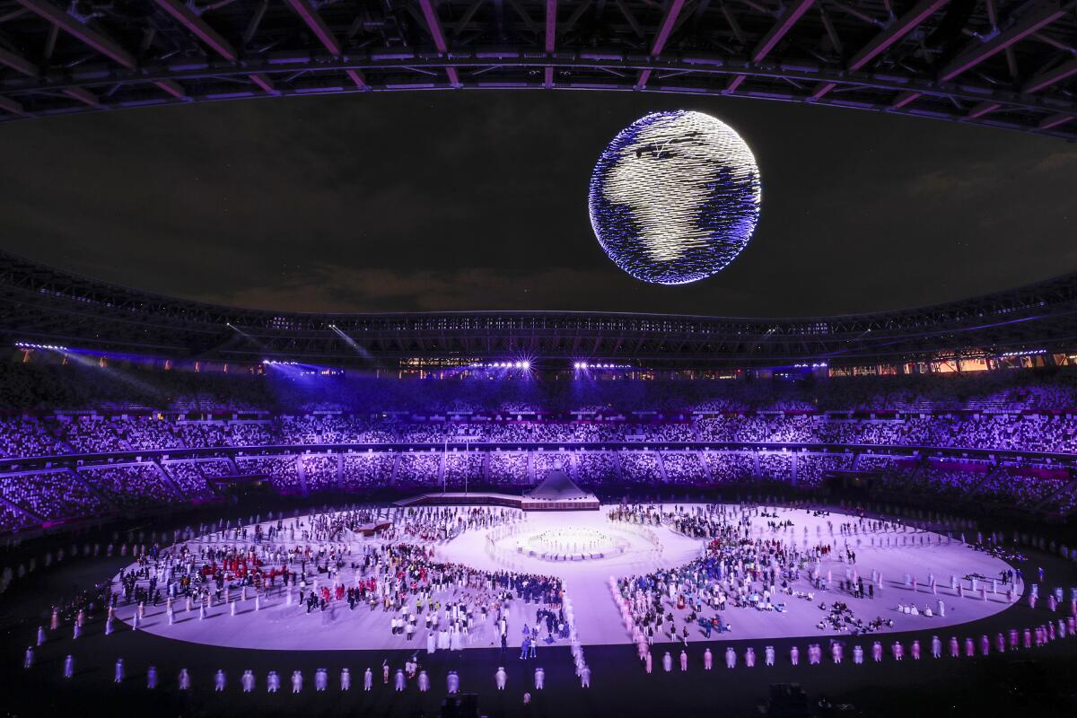 Lighted drones form the shape of a spinning earth over a crowd of people on the floor of the Olympic Stadium in Tokyo.