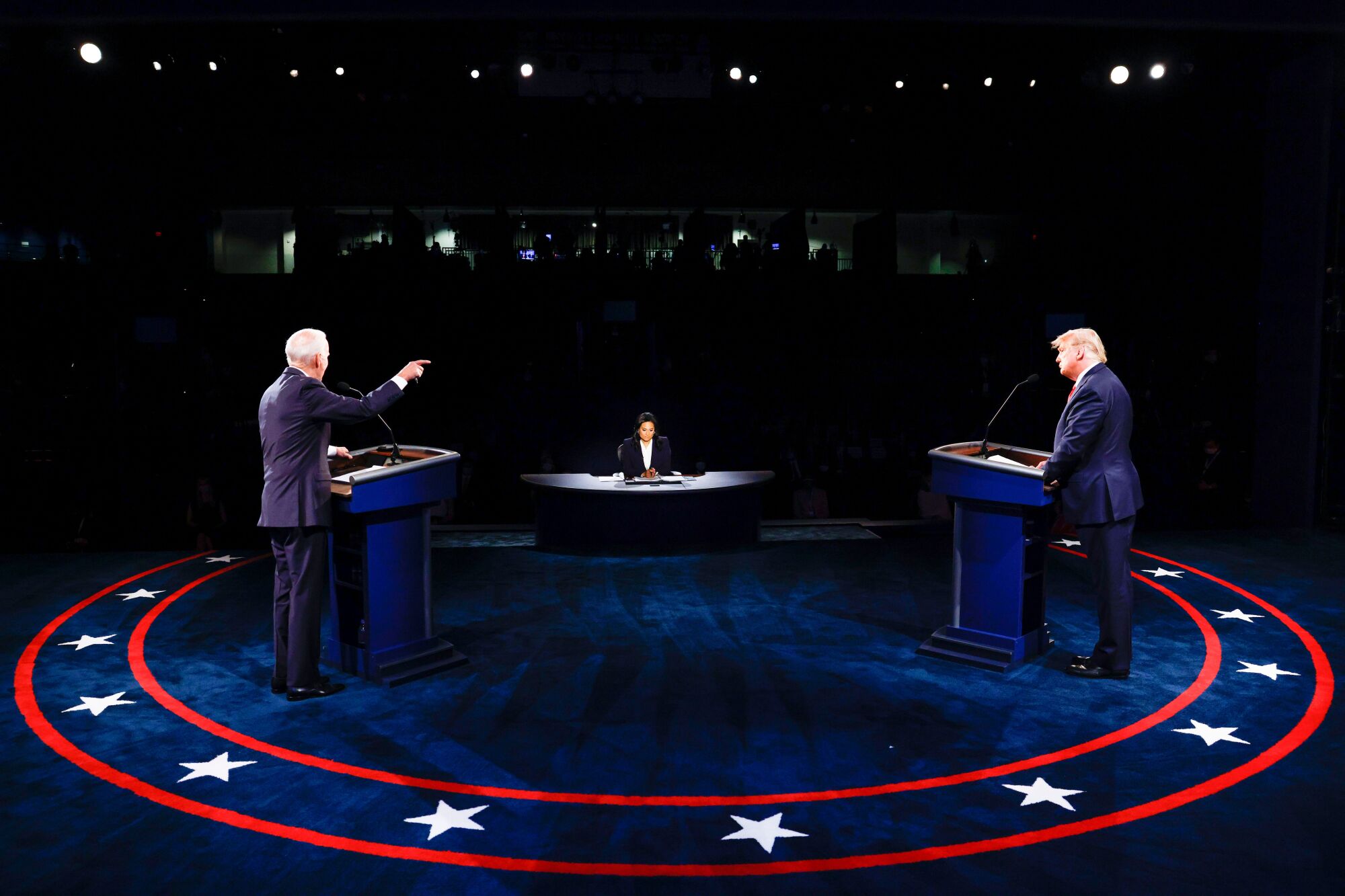 President Trump and Joe Biden stand at their lecterns on a blue-carpeted debate stage with the moderator seen between them