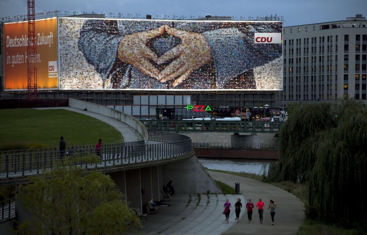 People run by a giant election billboard in Berlin featuring German Chancellor Angela Merkel's famous diamond-shaped hands pose. German voters go to polls Sunday for the general election.