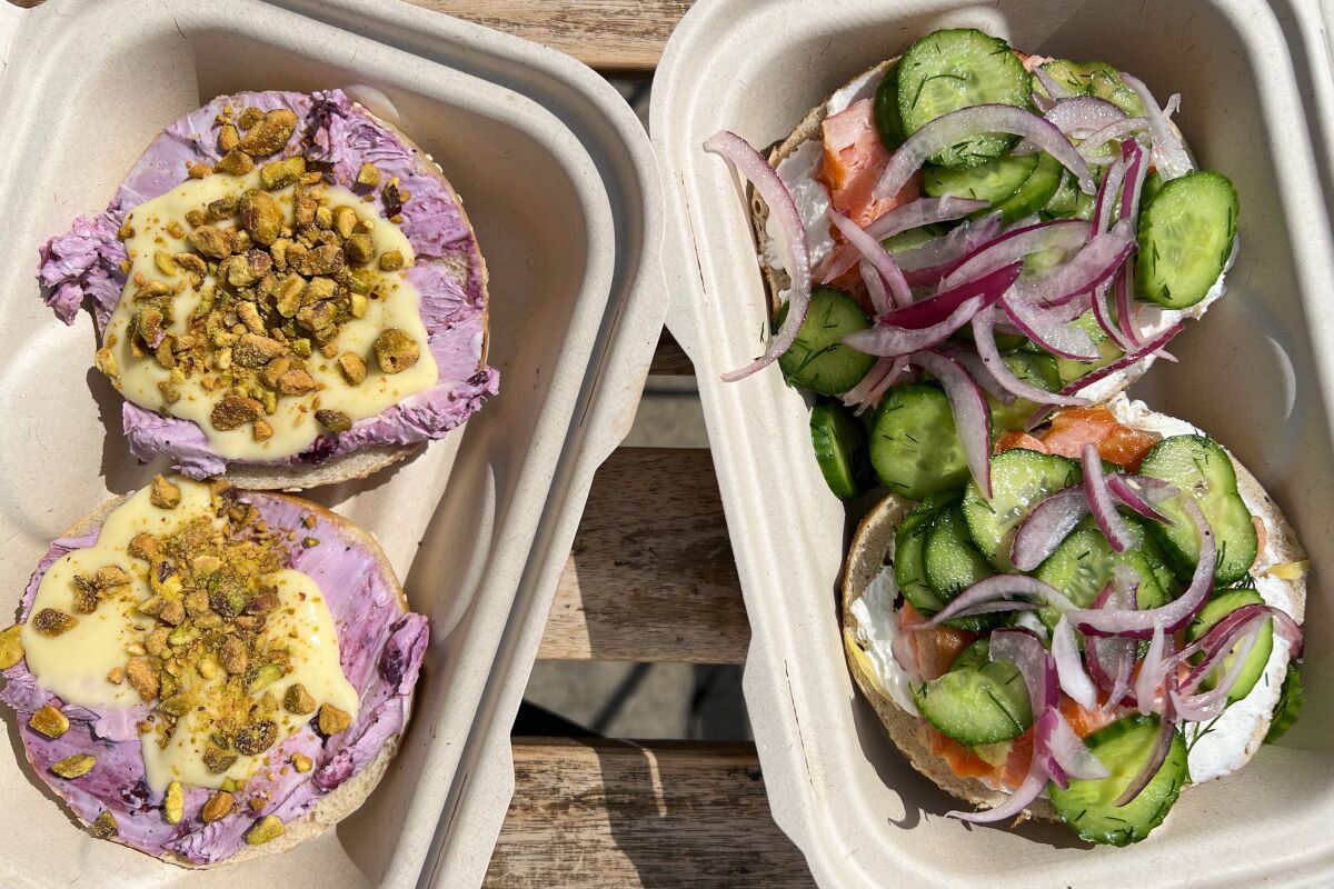 Bagels with various toppings, halved and in takeout containers.