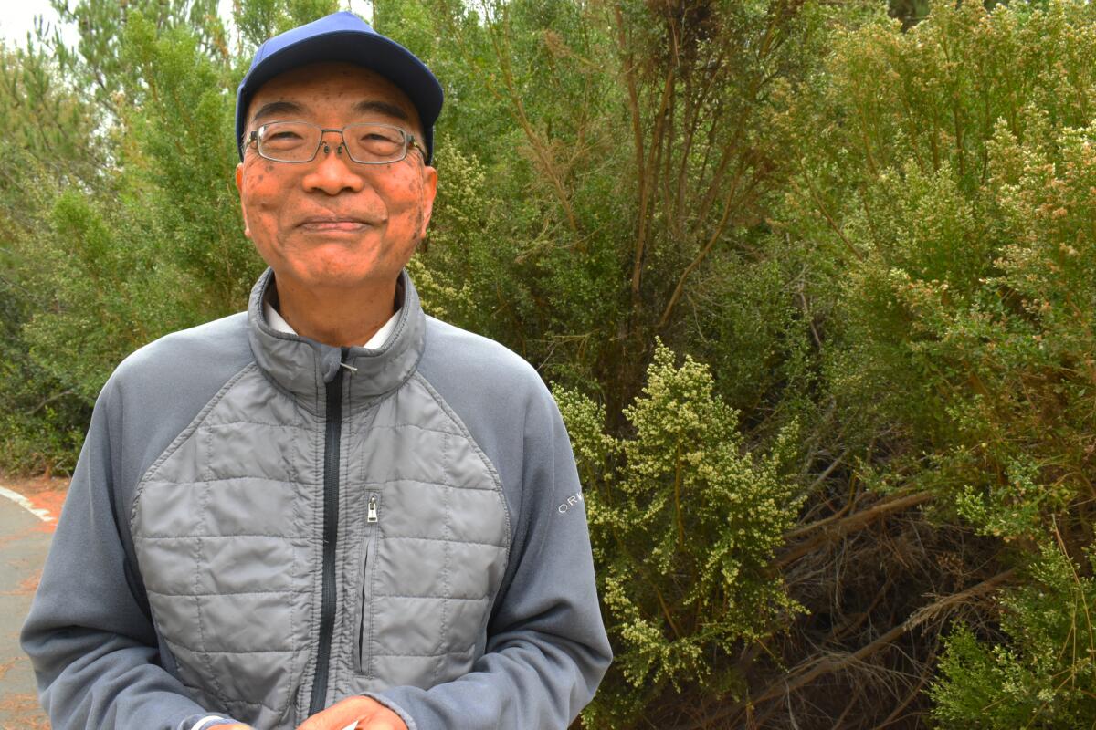 A man standing outside next to thick shrubbery 