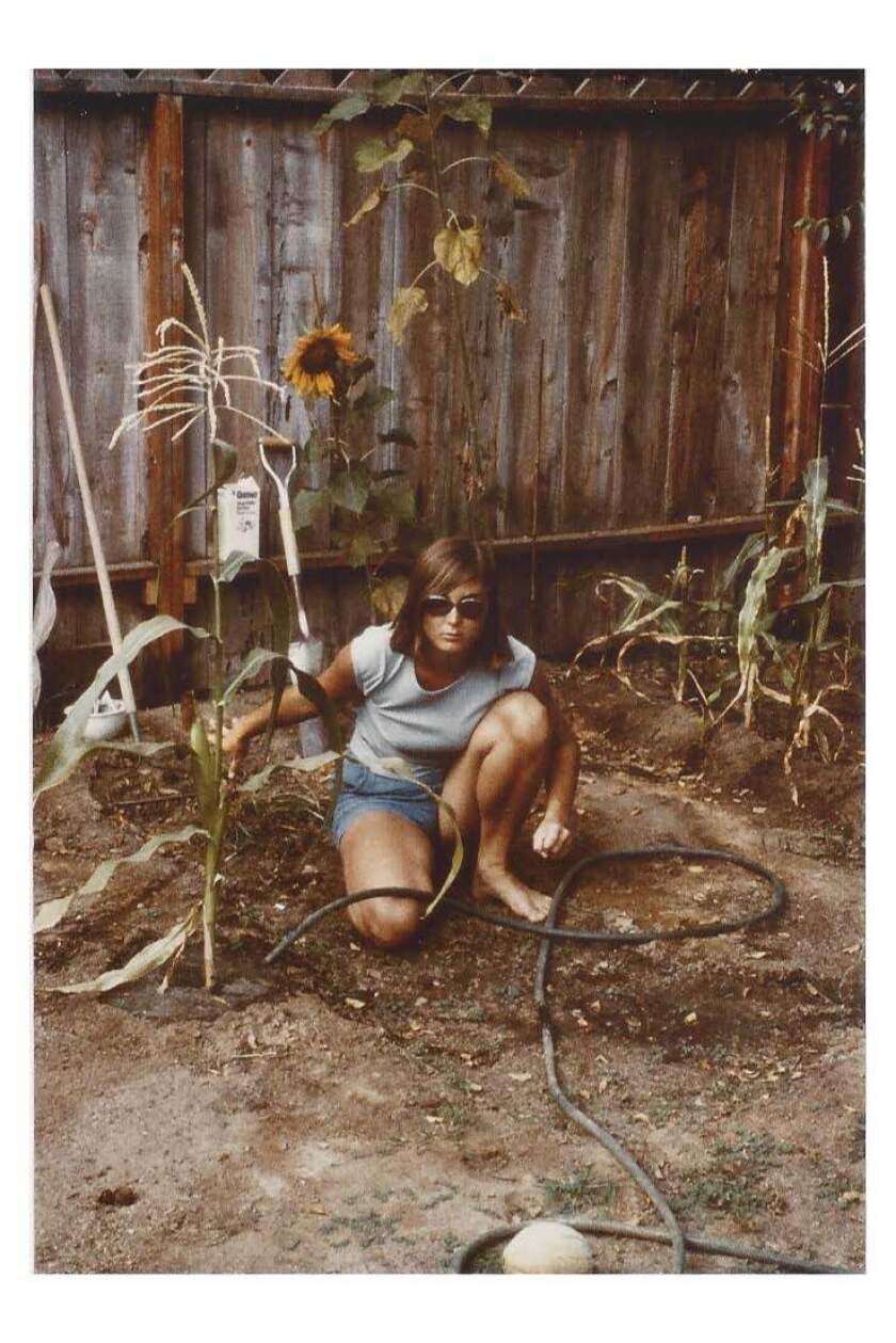 A woman in sunglasses and shorts squats down near the ground.