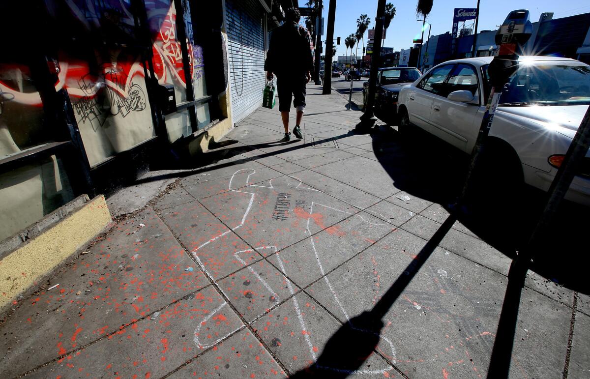 A pedestrian walks past an outline of a body drawn in chalk on the sidewalk in the 500 block of Fairfax Avenue in Los Angeles on Tuesday.
