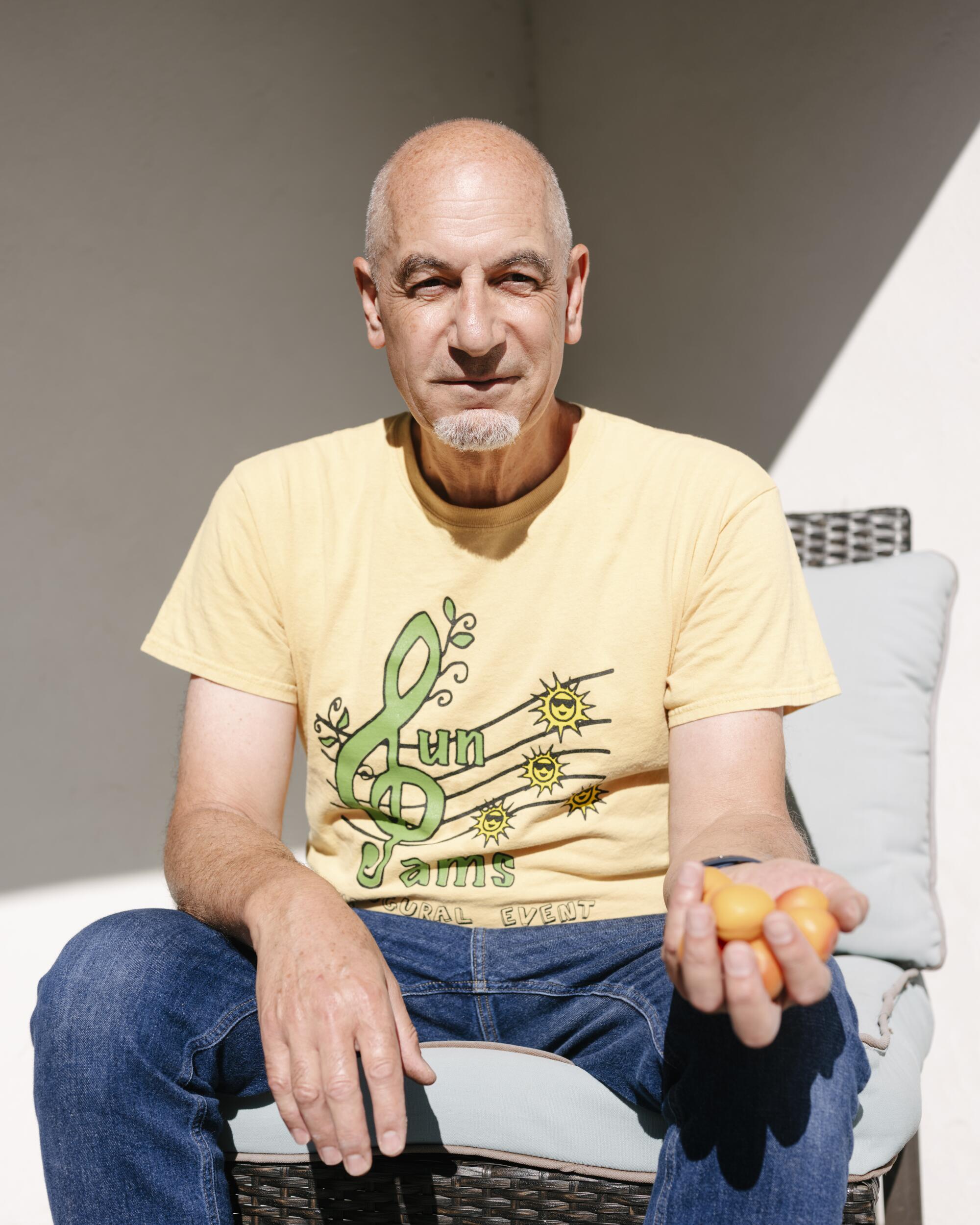A seated man in a T-shirt and jeans hold out a handful of apricots.
