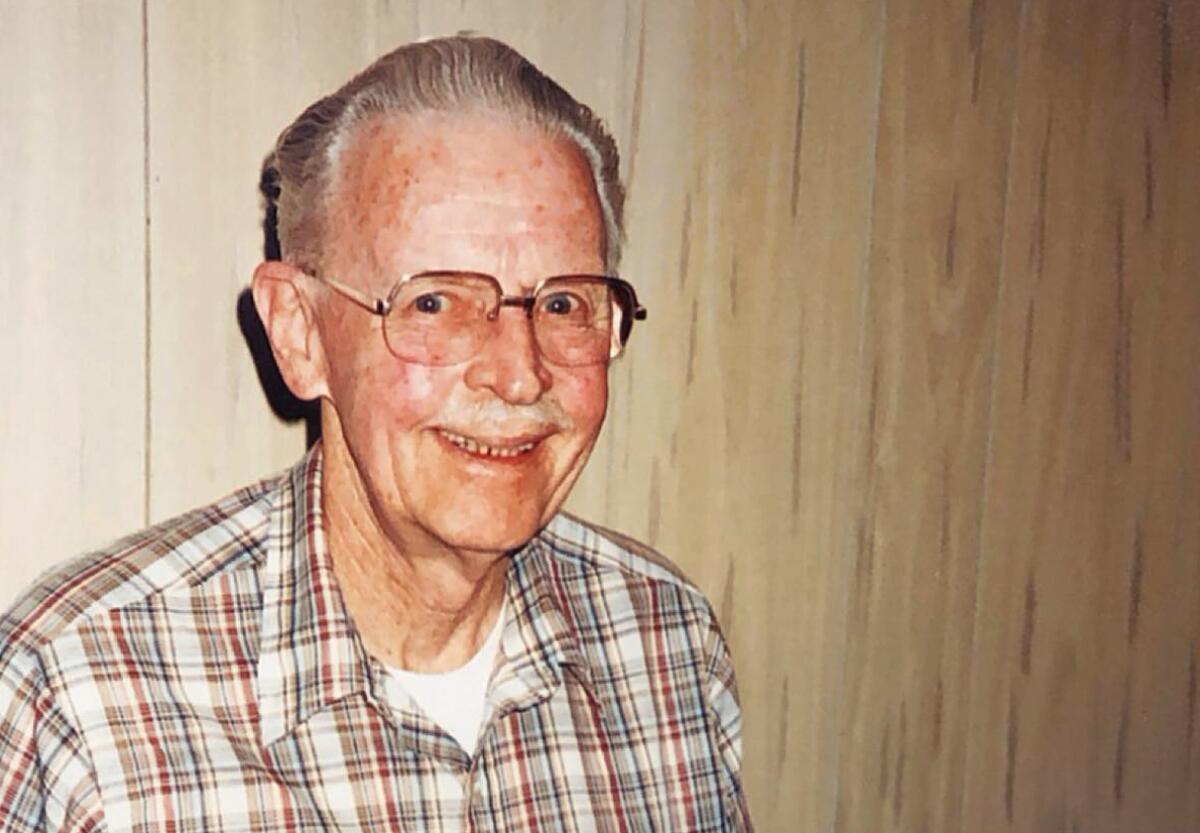 An older man wearing glasses and a plaid shirt open at the neck