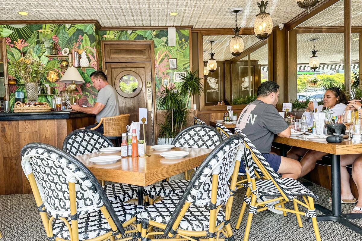 People sit on wicker chairs at wooden tables in a bright restaurant