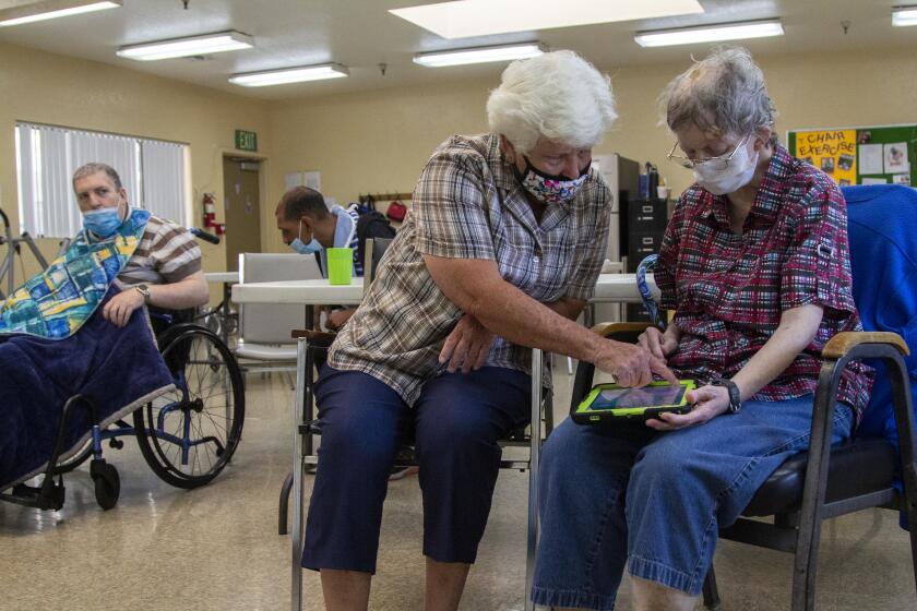 El Cajon, CA - July 12: Staff member Claudia Herbert helps Theresa Langford with an iPad in the exercise room at the Arc East County Training Center in El Cajon, CA. (Brittany Cruz-Fejeran / The San Diego Union-Tribune)