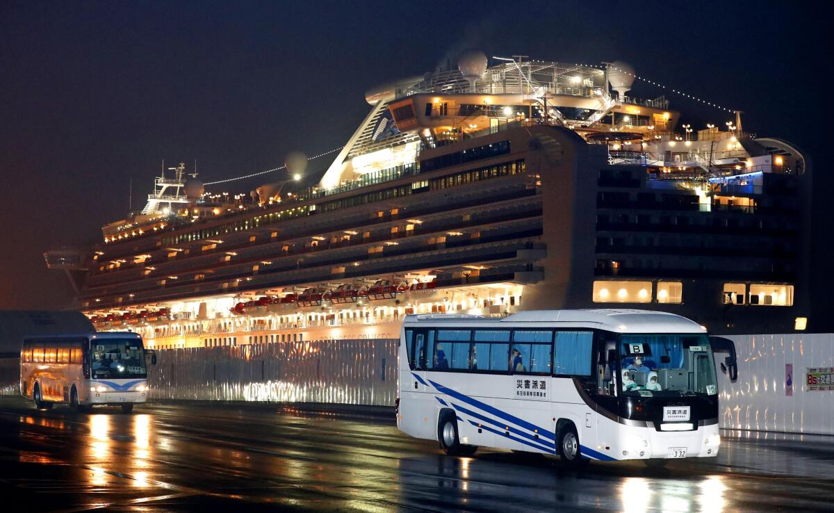 Buses carrying U.S. passengers who were aboard the quarantined cruise ship Diamond Princess, seen in the background, leave Yokohama, Japan, on Feb. 17. The cruise ship was carrying nearly 3,500 passengers and crew members under quarantine.