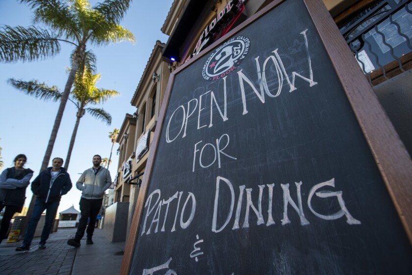 Pedestrians walk by a sign advertising patio dining 