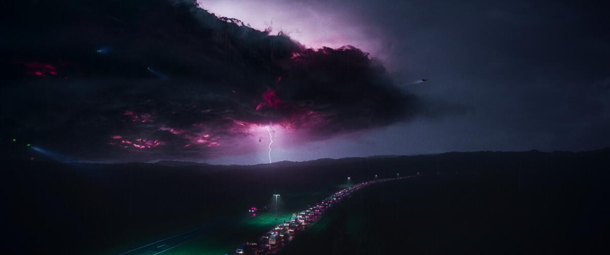 A line of cars on a dark highway and a view of purple lightning striking behind it 