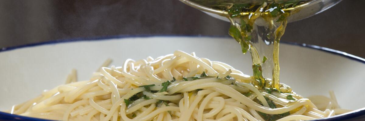 Oil being poured from a pot into a dish of pasta 