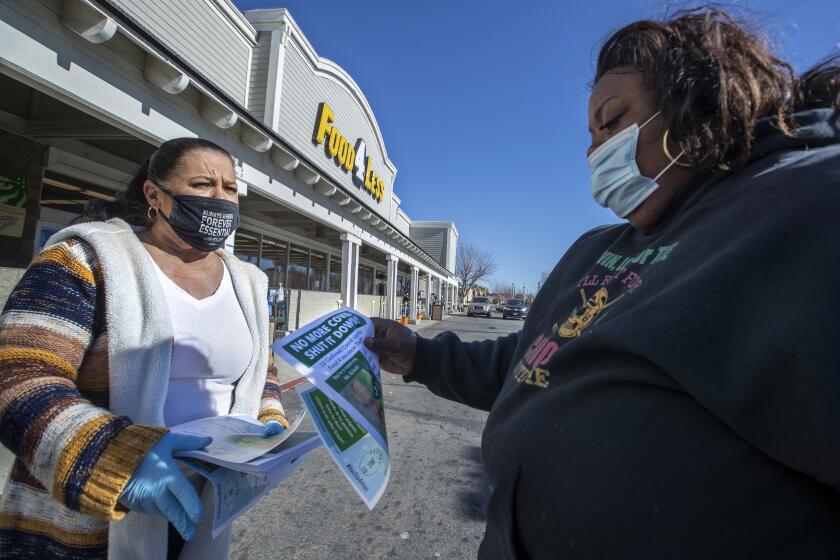 PALMDALE, CA - DECEMBER 18, 2020: Barbara Hughes, left, a cashier at Food 4 Less in Palmdale, hands a flyer to customer Rona Mllage of Palmdale, notifying her that there have been 22 confirmed cases of COVID-19 at this store in the past 2 weeks. Hughes demonstrated with others outside the store on December 18, 2020. (Mel Melcon / Los Angeles Times)