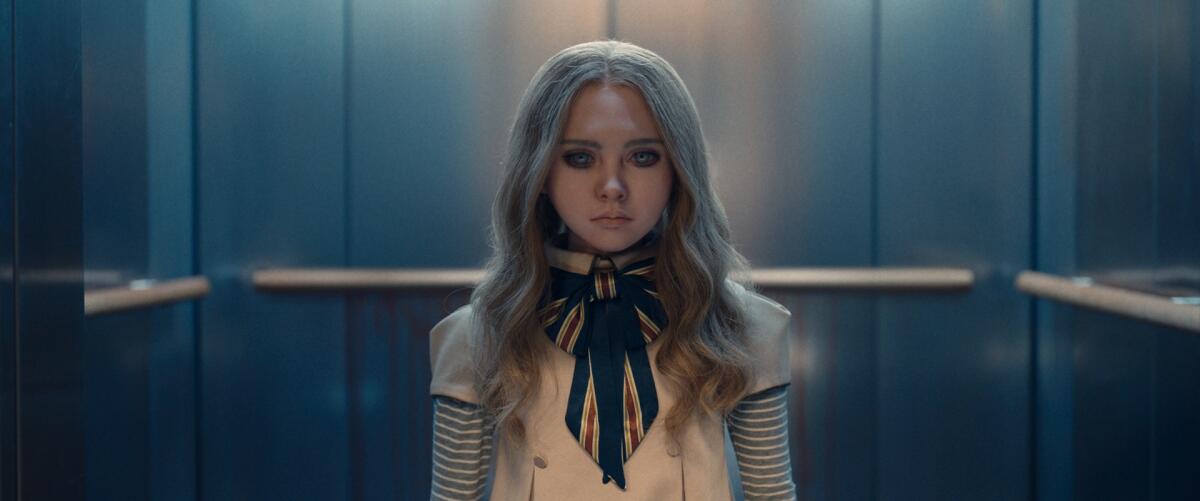 A creepy-looking young woman with long hair stands in an elevator, staring intently at the camera.