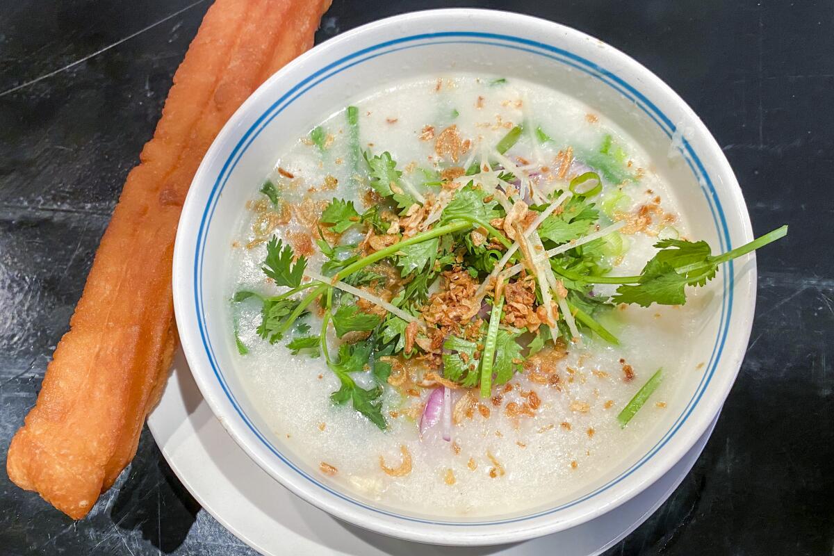 A bowl of rice porridge with a cruller on the side.