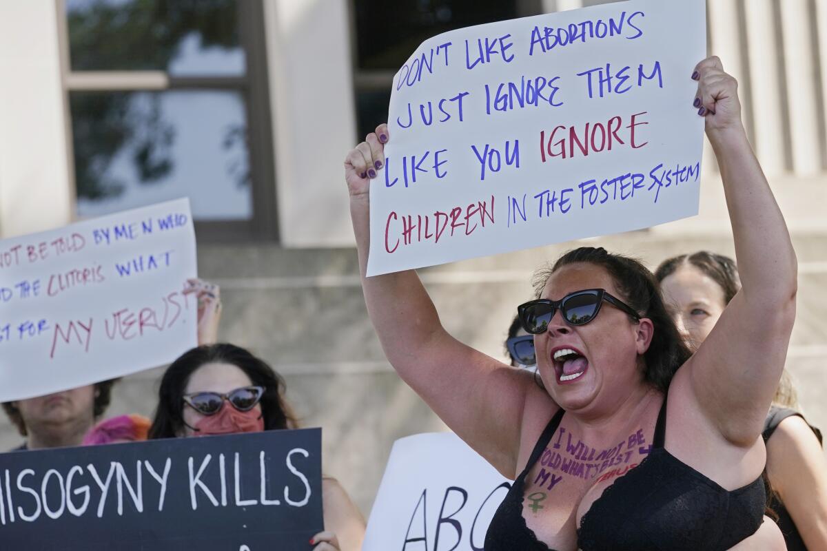 A woman holds a sign that reads "Don't like abortions just ignore them like you ignore children in the foster system."