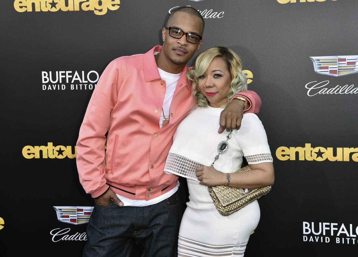 T.I. in a pink satin jacket posing with his right hand in his pants pocket. His left arm is around Tiny in a white dress