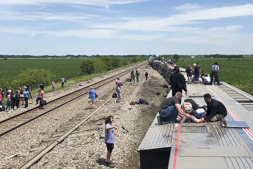 Passengers assist others climbing from a rail car on its side.