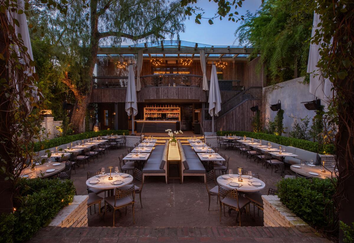 A restaurant's large open-air patio is dotted with trees and shrubbery at sundown