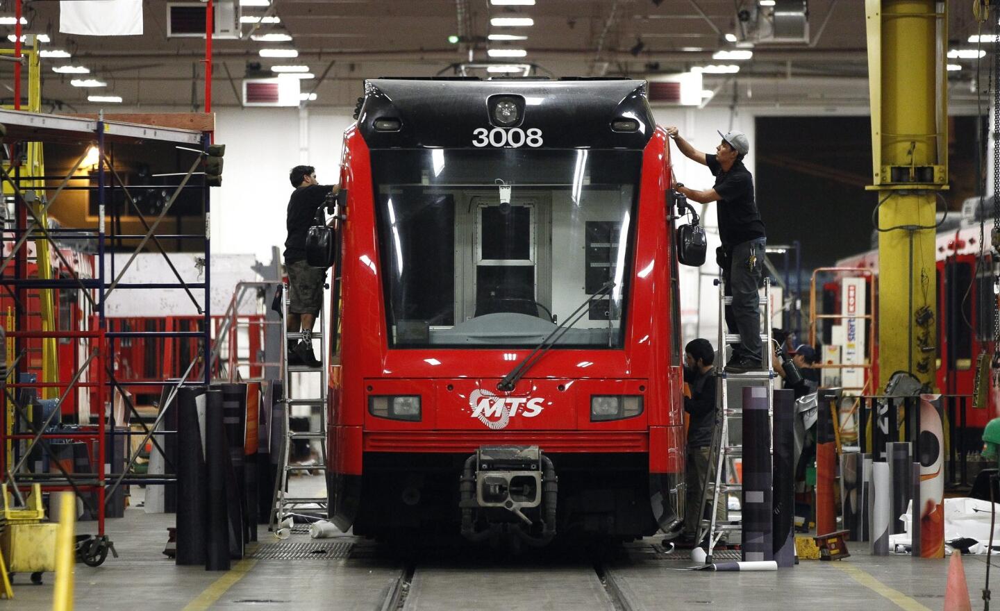 A crew works to wrap a trolley car with an advertising wrap in preparation for Comic-Con.