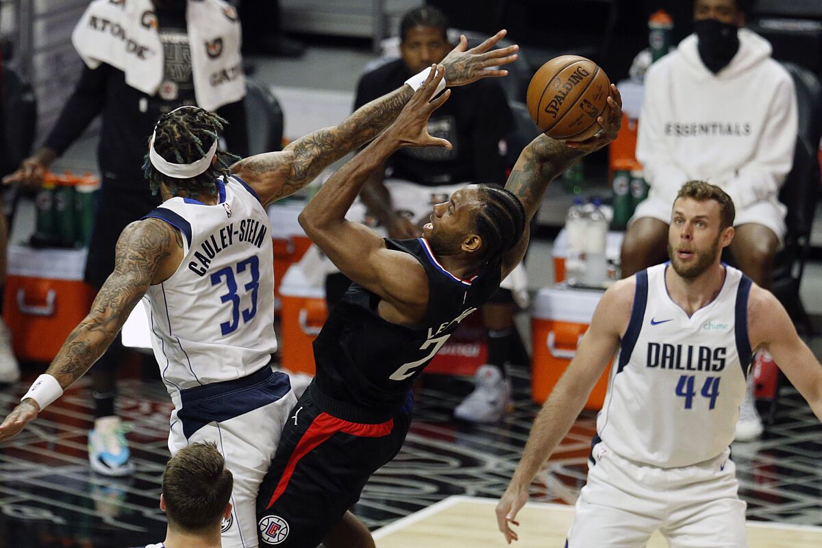 Clippers' Kawhi Leonard shoots while being guarded by Dallas Mavericks' Willie Cauley-Stein and Nicolo Melli.