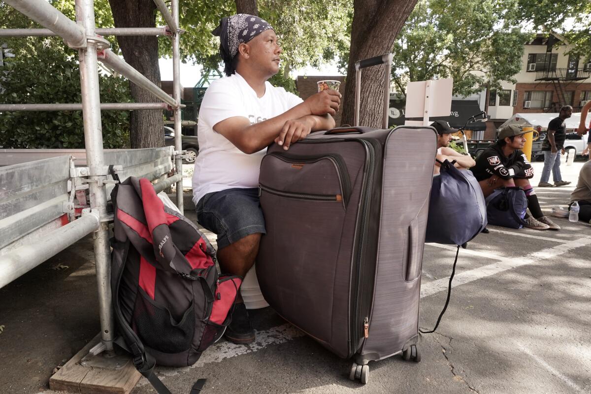 A man sits near a large suitcase and a backpack