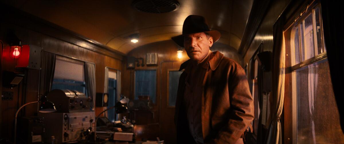 A man in a fedora stands in a train car