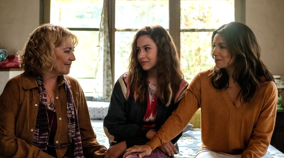 Three women sitting on a bed holding hands.