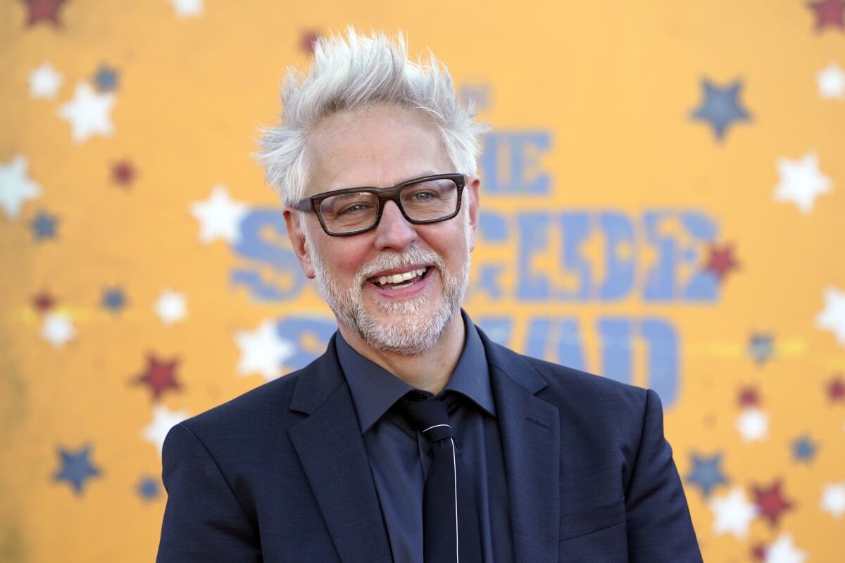 A man with white hair and a white beard smiling in glasses and a blue suit
