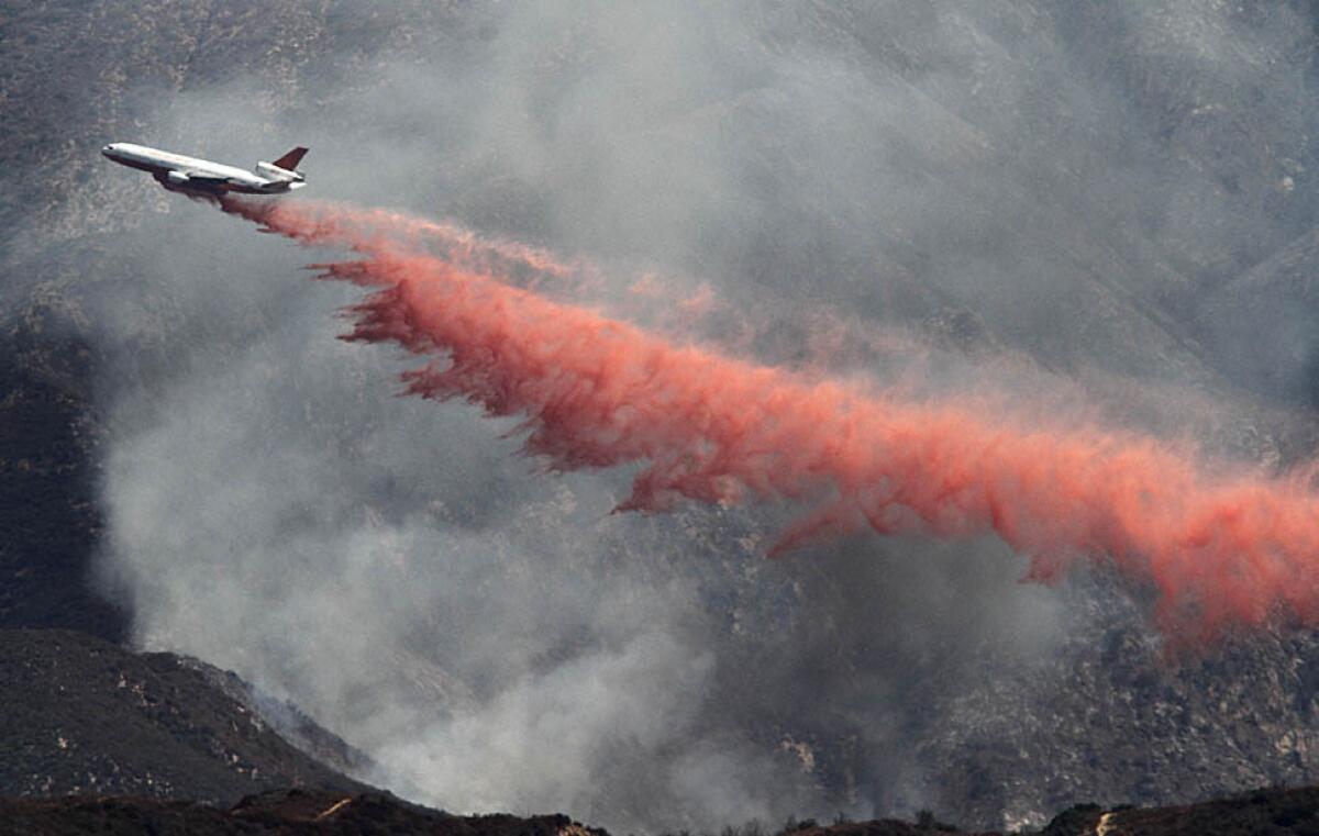 A DC-10 flies through a smoky valley and dumps a load of fire retardant on the Williams fire.