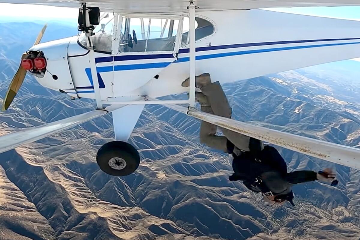 A person, wearing a parachute pack, is jumping out of a small plane.
