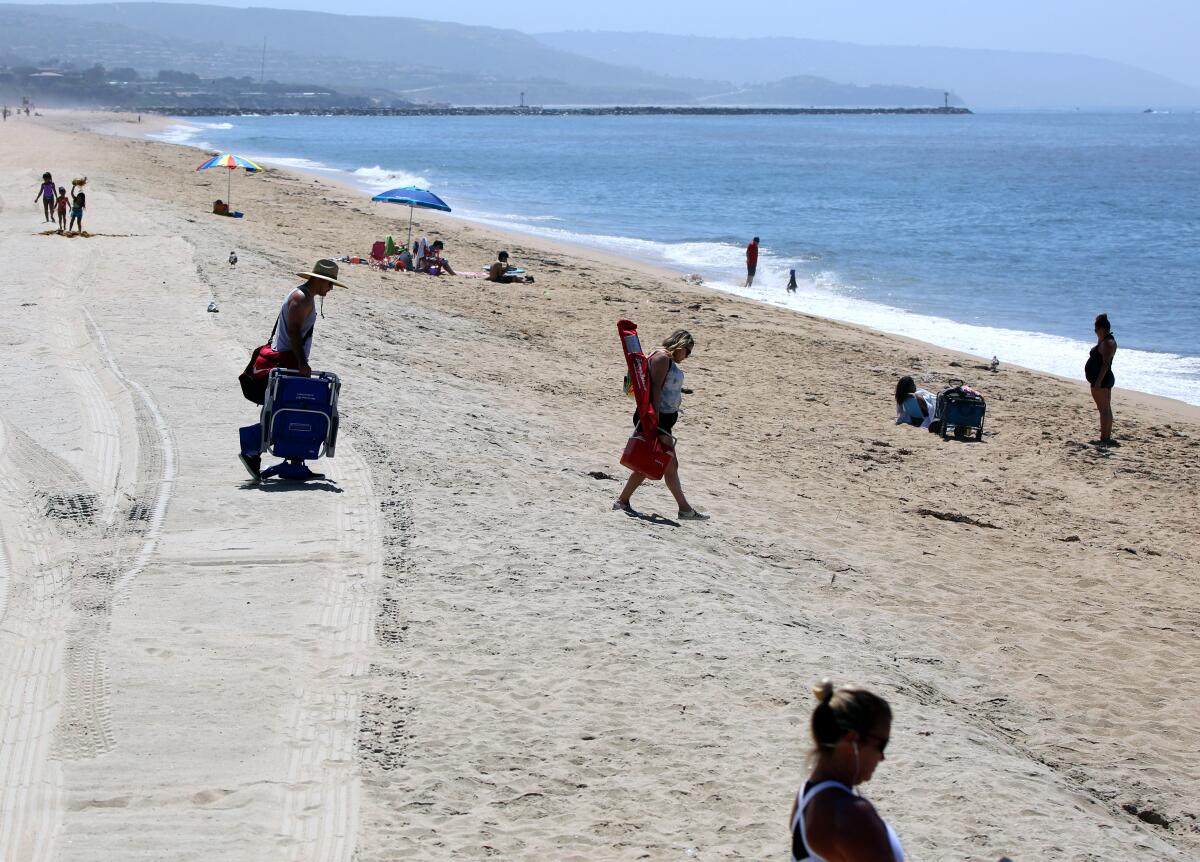 People arrive as others take in the sights on the beach next to the Balboa Pier in Newport Beach on May 6. The city is reopening some of its beachfront parking lots, starting with the smaller ones first.