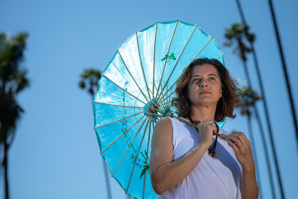 woman holds a sun umbrella in front of large palm trees 