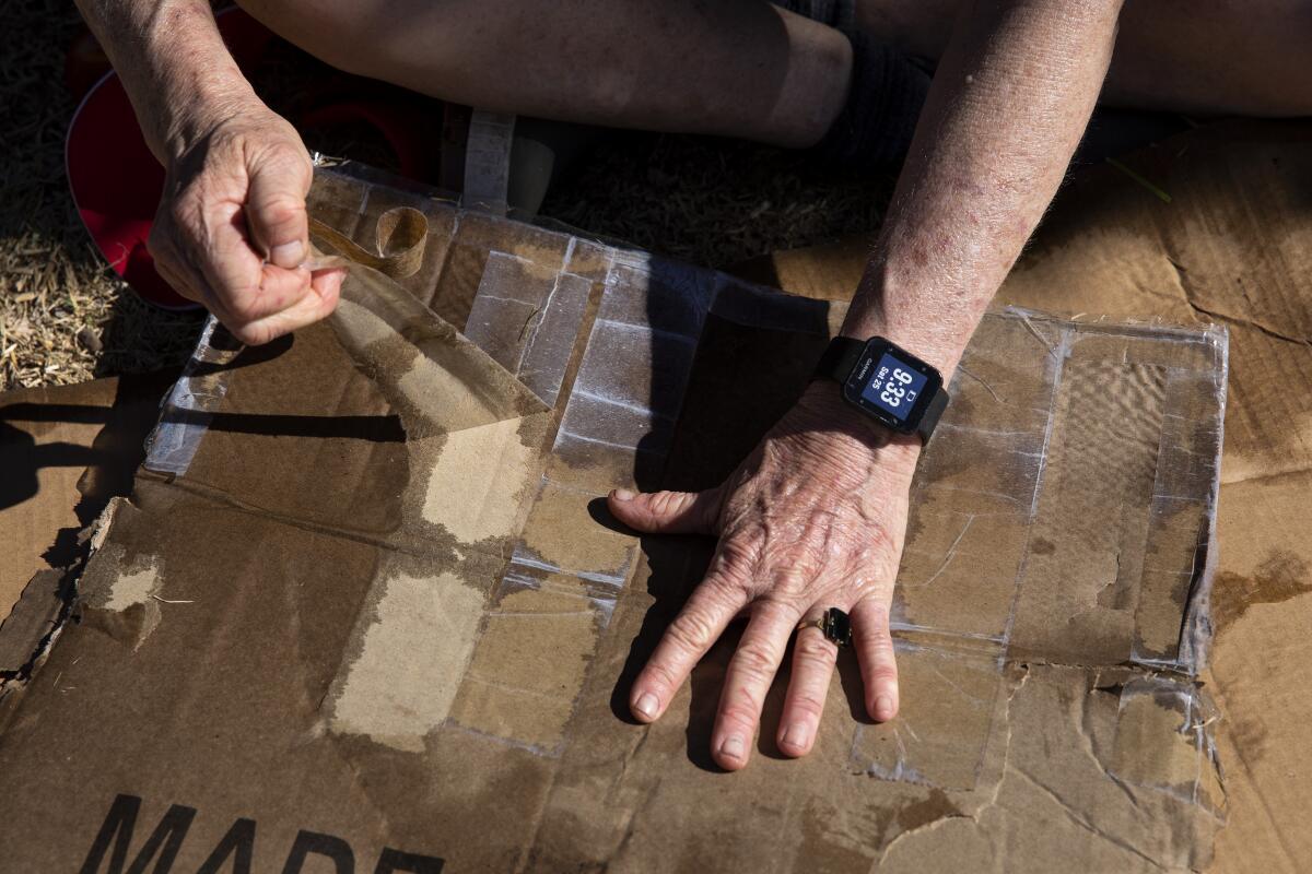 Photo of hands pulling a long piece of wide tape off a wet and flattened cardboard box.