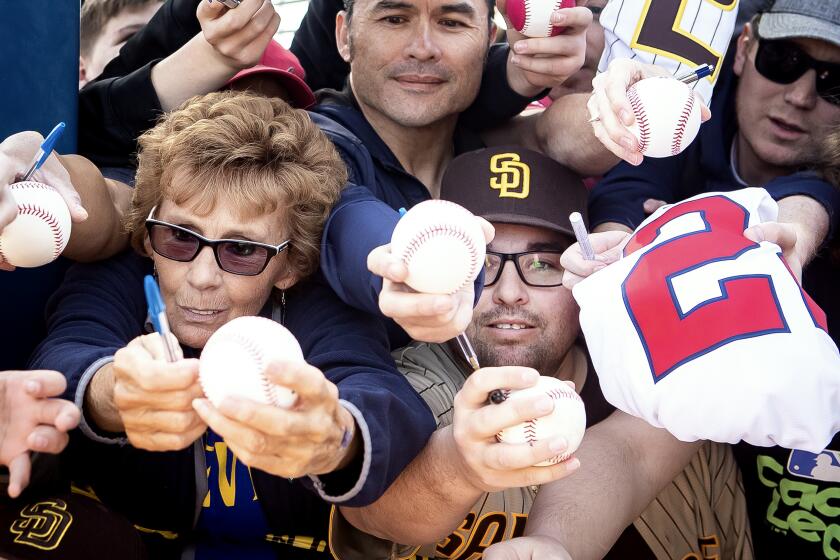 Peoria, AZ - February 18: Jane Henderson, of Sun City, left, and dozens of fans lean over each other to beg for Padres autographs during a spring training practice at the Peoria Sports Complex on Saturday, Feb. 18, 2023 in Peoria, AZ. (Meg McLaughlin / The San Diego Union-Tribune)