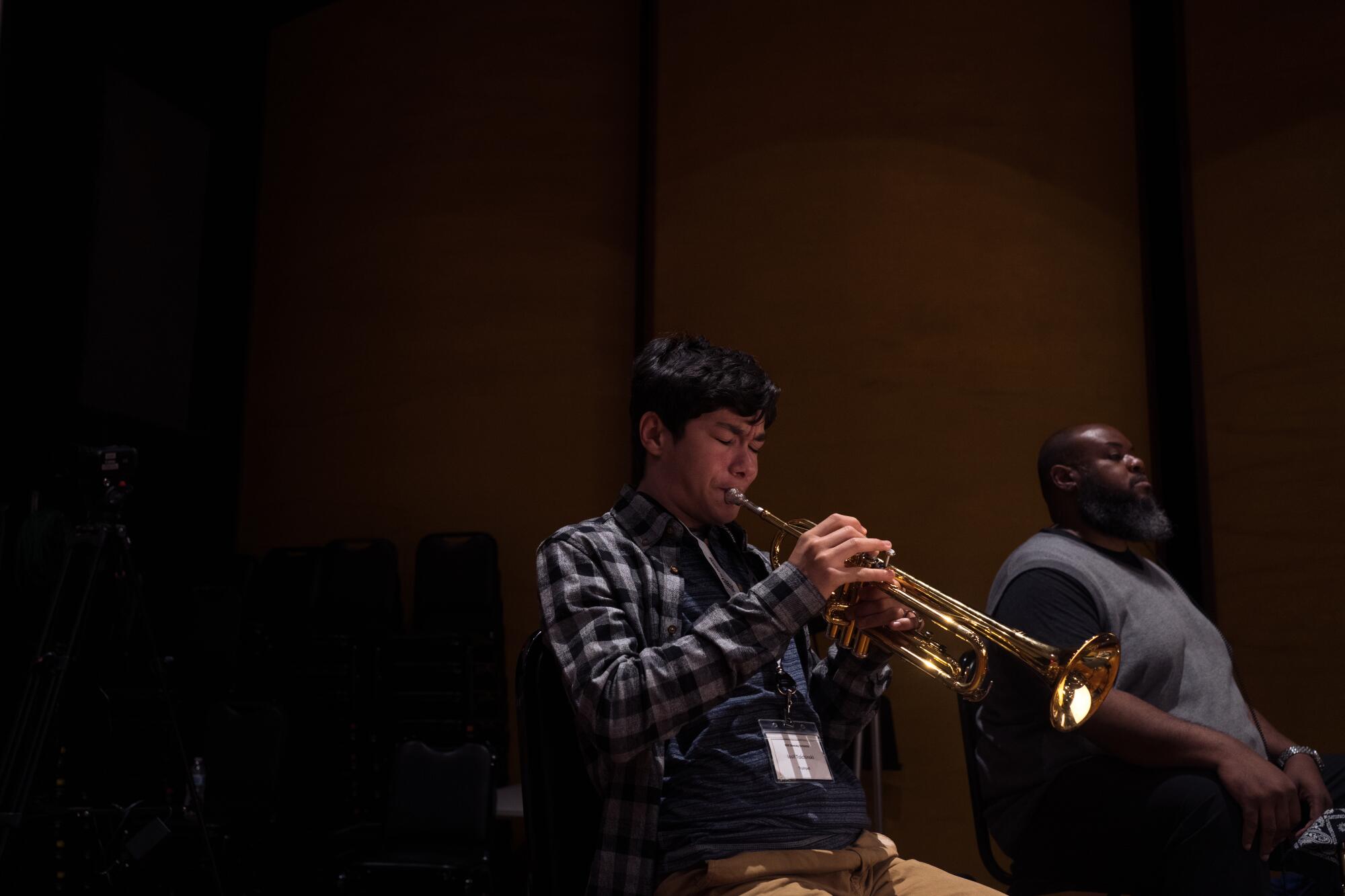 A young man plays the trumpet in a dark room.