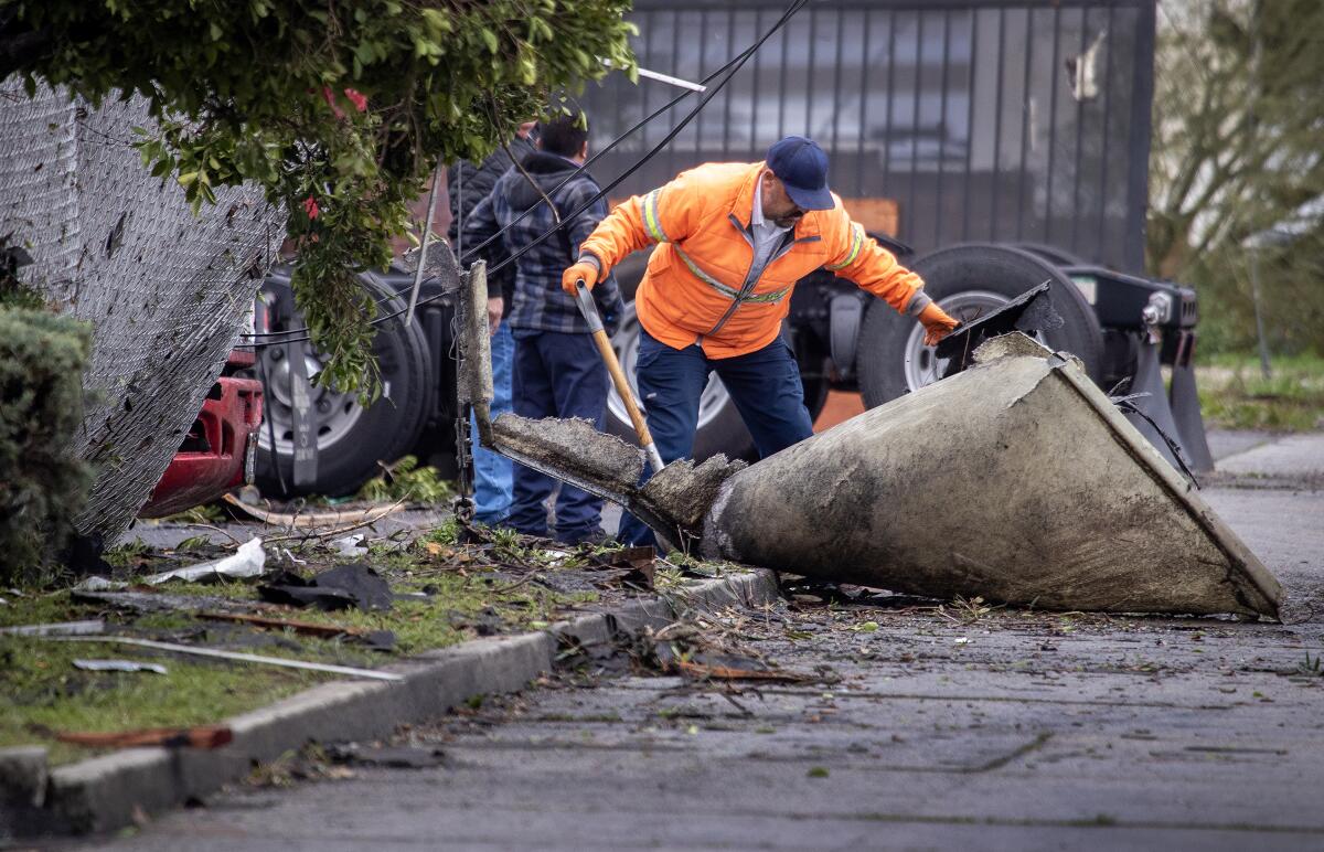 A man in a work jacket removes a large item from the side of a street strewn with debris