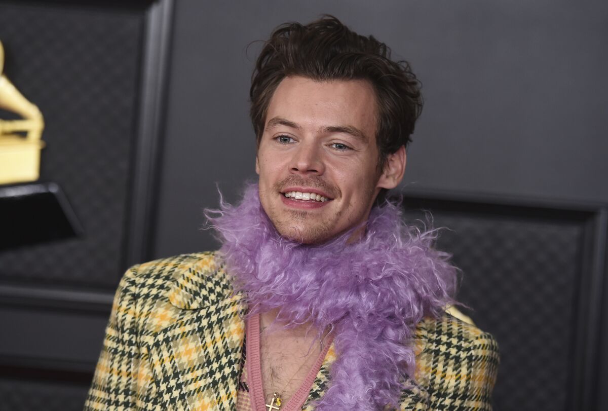 A smiling man in a yellow checkered jacket and a purple boa