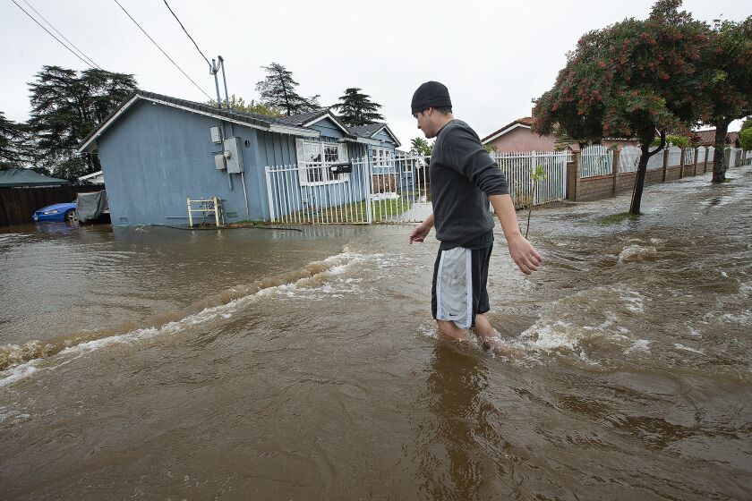 MISSION HILLS, CA-DECEMBER 4, 2019: Mission Hills resident Alberto Rodriguez, 32, walks through knee deep water on a flooded street outside of his home, at left, on Woodman Ave. The cause of the flood was a rupture from a 72 inch steel riveted trunk line that was installed back in 1914. (Mel Melcon/Los Angeles Times)