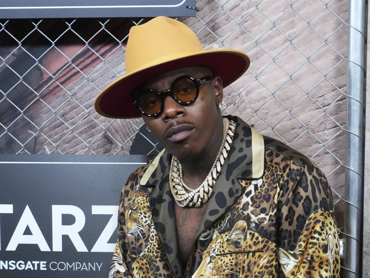 A man in sunglasses, a hat, gold chains and an animal print jacket