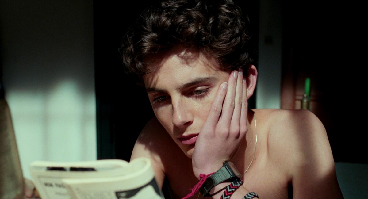 A shirtless young man reads in "Call Me By Your Name."