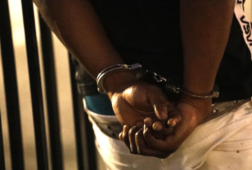 A man is detained and placed in handcuffs while Los Angeles police officers search the car he was riding in.