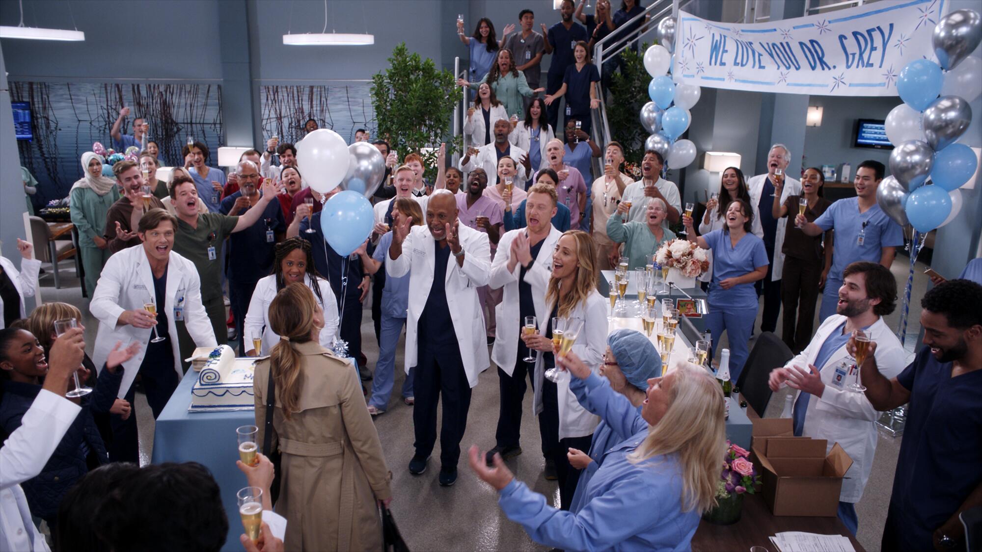 Many doctors and nurses clap at a surprise party at a hospital.
