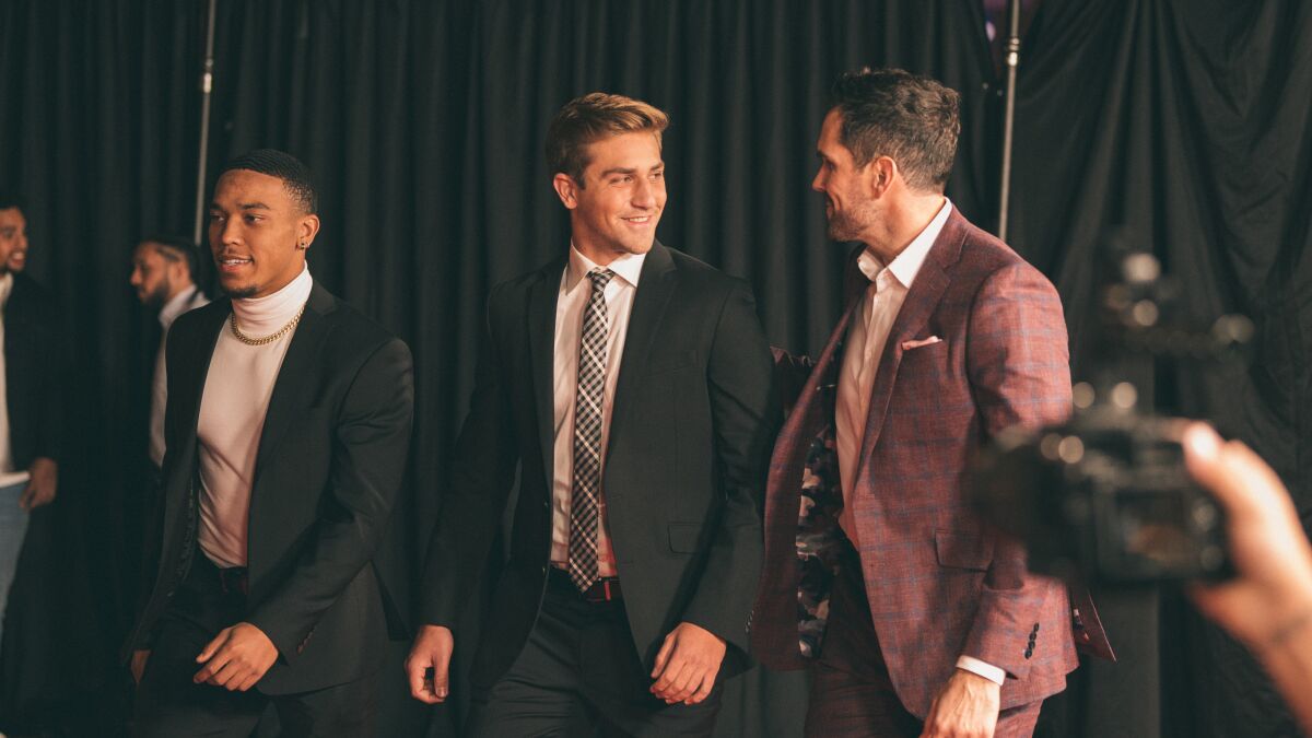 Amon-ra St. Brown, Kedon Slovis and Matt Leinart, in suits, walk and chat.
