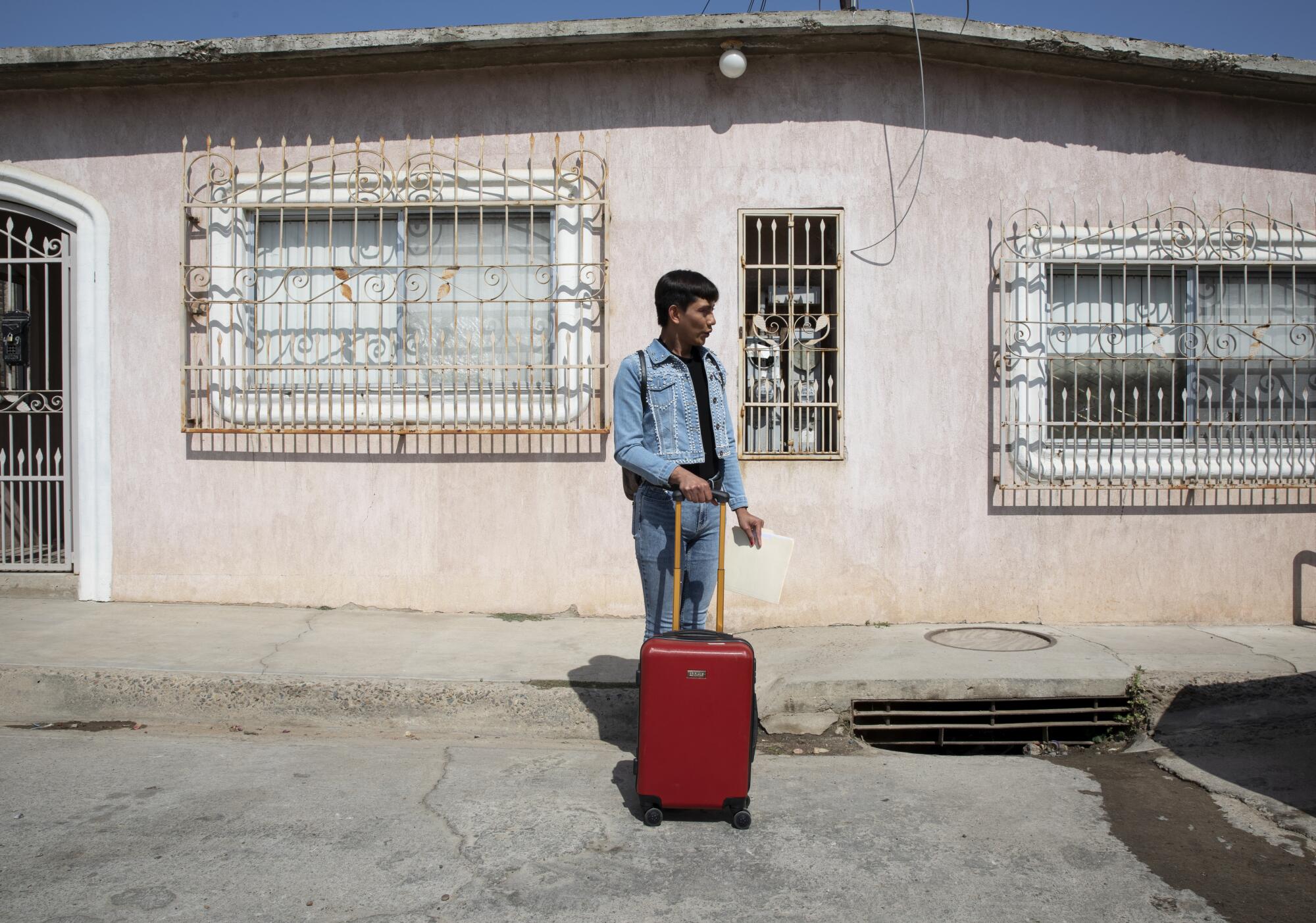 Ceidy Zethare stands on the street holding her red suitcase