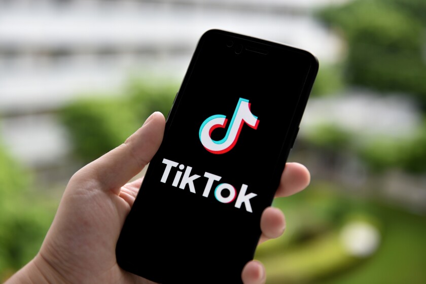 A hand holding a smartphone with the TikTok logo on the screen