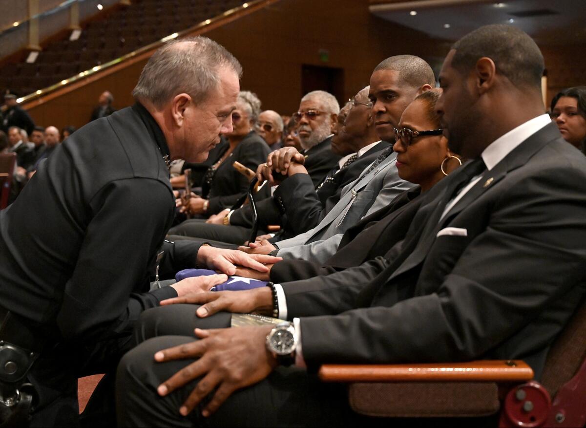 LAPD Chief Michel R. Moore hands the flag that was draped over the casket of former LAPD First Assistant Chief of Operations Earl C. Paysinger to his wife Miguel as sons Brian and Steven look on.